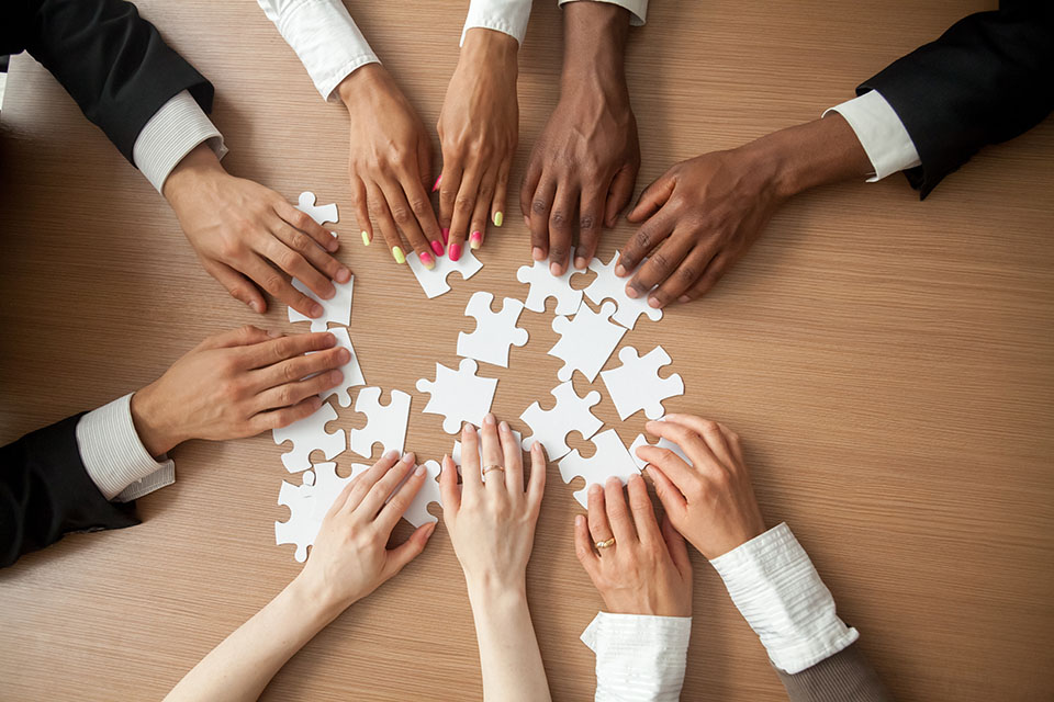 Hands of diverse people connecting puzzle together on office desk, multi-ethnic team engaging in finding best business solutions for successful teamwork, teambuilding unity concept, top close up view